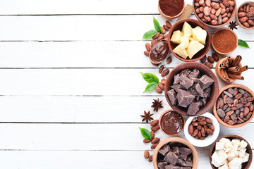 Cocoa beans, chocolate, cocoa butter and cocoa powder on a white wooden background. Top view. Free copy space.