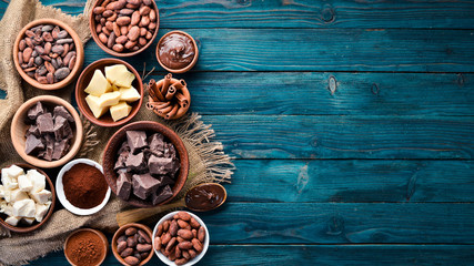 Chocolate, cocoa and cocoa beans on a blue wooden background. Top view. Free copy space. - obrazy, fototapety, plakaty