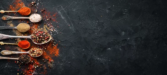 Poster Peper in een lepel. Gekleurde peper, zeezout, gemalen peper, Spaanse peper. Bovenaanzicht. Op een zwarte achtergrond. © Yaruniv-Studio