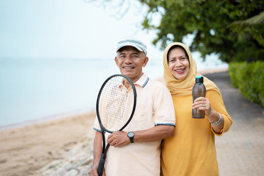 Senior Asian Man And Woman Smiling With Racket Tennis