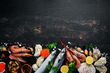 Seafood. Fresh fish, shrimp, oysters and caviar on a black wooden background. Top view. Free copy space.