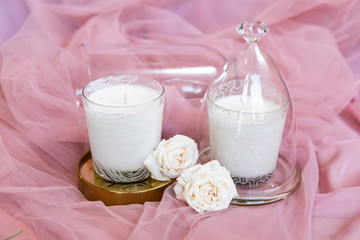 scented candles under glass case with flowers on pink textile background.
