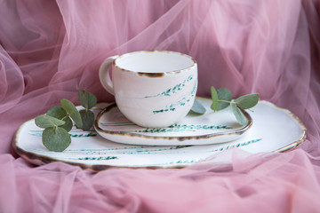 Ceramic Cup and trays decorated with floral ornaments and green branches close up