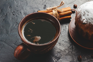 Cup with hot coffee, muffins and cinnamon sticks on the dark, textured background