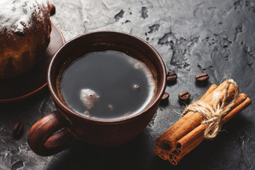 Cup with hot coffee, muffins and cinnamon sticks on the dark, textured background