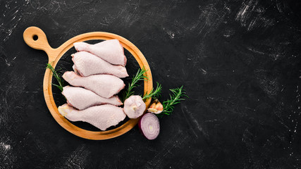 Raw chicken legs and spices and herbs. Barbecue. On a black stone background. Top view. Free copy...