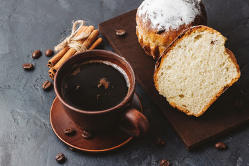 Cup with hot coffee, muffins and cinnamon sticks on the dark, textured background