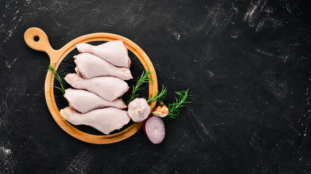 Raw chicken legs and spices and herbs. Barbecue. On a black stone background. Top view. Free copy space.