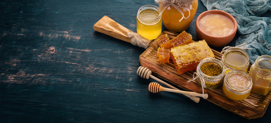 A set of honey and bee products. Honey in honeycomb. On a black wooden background. Free space for...