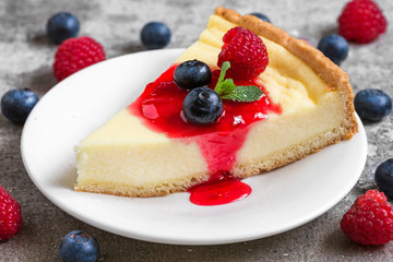 slice of cheesecake with fresh raspberries, blueberries, jam and mint on concrete background. close up
