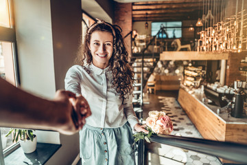 Portrait of beautiful woman with bouquet flowers. Her boyfriend holding hand when they climb the stairs of the restaurant.