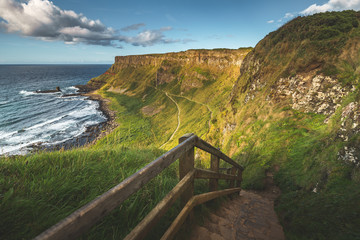 Rock stairs leading to the shore. Northern Ireland landscape. Overview of the stunning Irish shoreline. Grass covered cliffs next to the ocean. Close-up touristic trail among the wild nature.