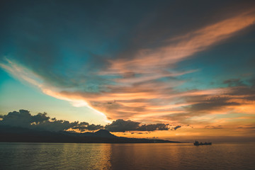 Colorful bright sunset sky over the Komodo island shore. Indonesia. Picturesque landscape. The clouds reflection on the calm water surface. The lone ship sailing into the distance. Fairy tale scene.