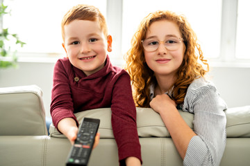 Happy girl and boy watching tv with remote control