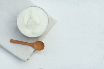 Fototapeta na wymiar Plain yoghurt in white bowl and wood spoon on white wooden table background