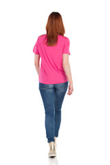 Rear View Of Walking Young Woman In Pink Shirt, Jeans And Gold Sneakers