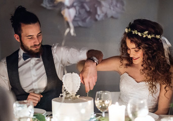 A young couple sitting at a table on a wedding, cutting a cake.