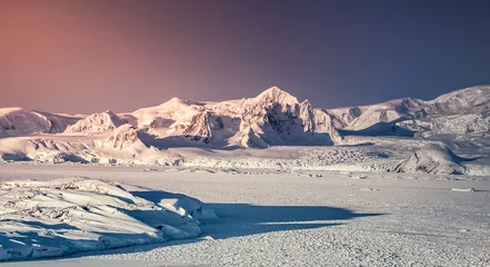 Sonnenuntergang in der Antarktis. Schnee auf der Bergkette gegen bunten rosa und blauen Himmel. Davor großer Gletscher. Naturhintergrund. Atemberaubende Winterlandschaft. Die Wildnis. Schönheit des wilden Südpols © Goinyk