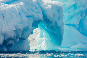 Close-up arch of the iceberg. Antarctic landscape in the blue and white tints. Overwhelming scene of the ice covered glacier floating among the polar ocean. The geometric shapes of the ice mount. - obrazy, fototapety, plakaty