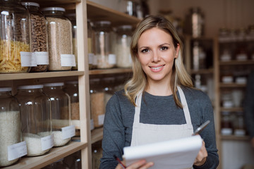 A female shop assistant with smartphone working in a zero-waste shop.