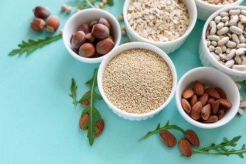 Set of bowls with organic quinoa, lentil, chickpea, wheat, walnut, almond, hazelnut and sesame. Cereals and legumes assortment on blue paper background. Top view. Copy space. Flat lay