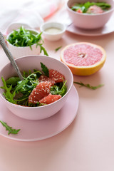 Fresh citrus salad with arugula, grapefruit and sesame seeds on pink background. Selective  focus. Raw vegetarian spring detox food.