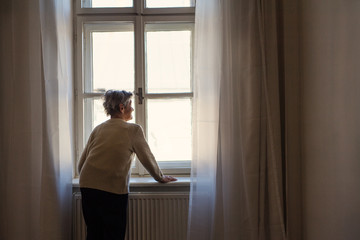 Fototapeta na wymiar A portrait of a senior woman standing at home, looking out of a window.
