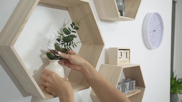 woman puts decor and flowers on the shelves on the wall