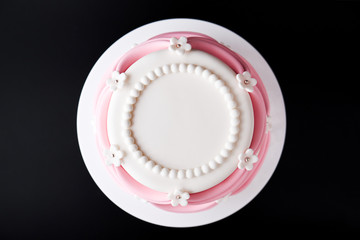 White wedding cake with pink elements made from pastry mastic on a black background. Top view. Sugar flowers, marzipan flowers and mastic, beautiful decor for decorating cakes. Close-up.