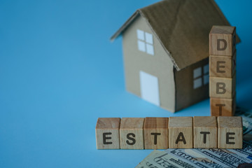 House model and debt estate wording on wooden cubes on blue background.Saving and investment to real estate concept. -image.