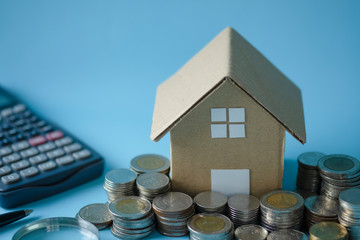 House model around with stacking coins money calculator on blue background. Saving and investment to real estate concept. -image.