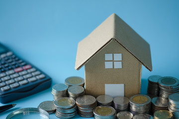 House model around with stacking coins money calculator on blue background. Saving and investment...