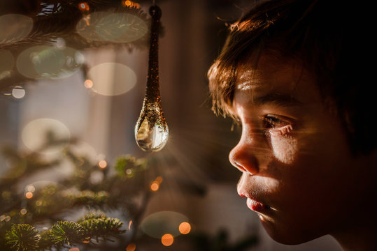 Boy looking at a crystal ornament hanging on a Christmas tree