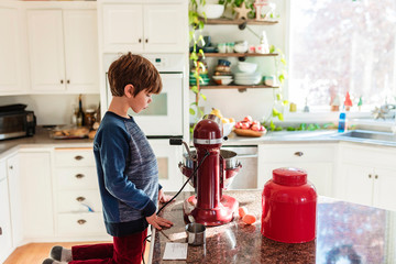 Boy kneeling on stool in the kitchen making a cake