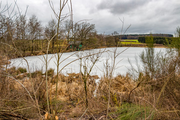 The February frozen pond of the village of Thommen, Belgium with a cabin