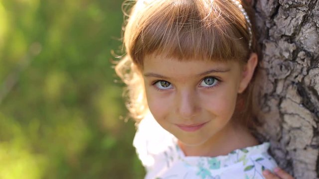 Portrait of a cute little girl in the Park on the grass next to the big tree, her eyes are different colors. Portrait of a small child with heterochromia.