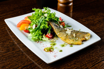 Appetizing tasty baked fish served with tomatoes, oranges and spices in the white plate
