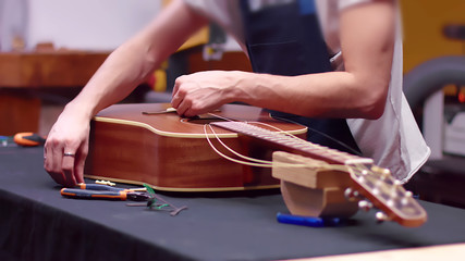 Luthier changes the strings of an acoustic guitar