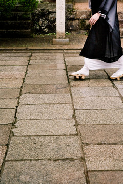 Buddhist monk wearing traditional wooden Geta sandals walks along a stone pathway.