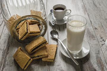 biscotti farciti al cioccolato fondente con tazzina da caffè e bicchiere latte