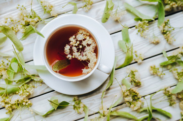 White cup of linden tea on linden blossom background. Herbal medicine. Top view. Treatment of cold and flu.