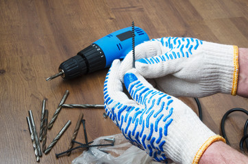 Man holding a screw,blue electric skrewdriver,drills on wooden floor.Concept of repair indoor