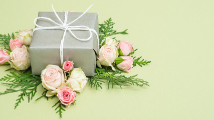 Holiday present. Silver gift box on palegreen background. Flower and foliage decor