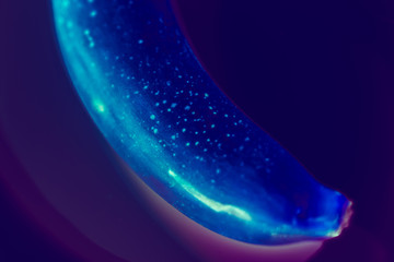 Conceptual art. Vivid glow design. Banana on purple gradient background close up.