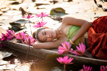 Obraz na płótnie Canvas young asian women in traditional dress in the boat and pink lotus flowers iin the pond. Beautiful girl in traditional costume, Thai girl in retro Thai dress. 