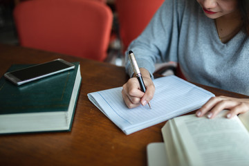 Young asia student study in the public library, She making note on notebook...