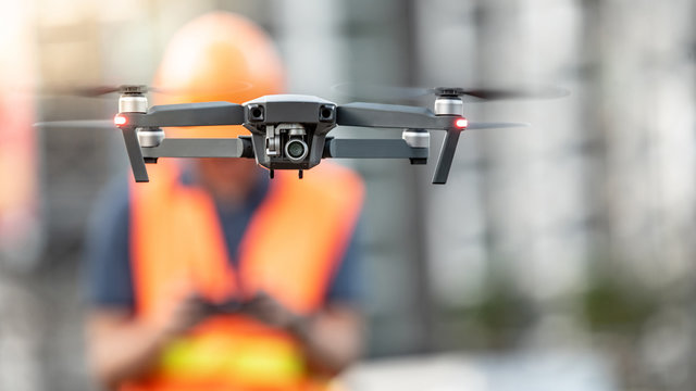 Asian engineer man or male worker flying drone over construction site. Using unmanned aerial vehicle (UAV) for land and building site survey in civil engineering project.