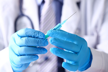 Physician arms wearing protective blue gloves prepare syringe