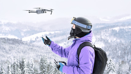 Male snowboarder in the violet jacket and black helmet launching a flying drone with a remote controller in his hand on winter mountain - Powered by Adobe
