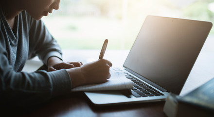 Young asia student study in the public library, She making note on notebook and using laptop. © ibravery